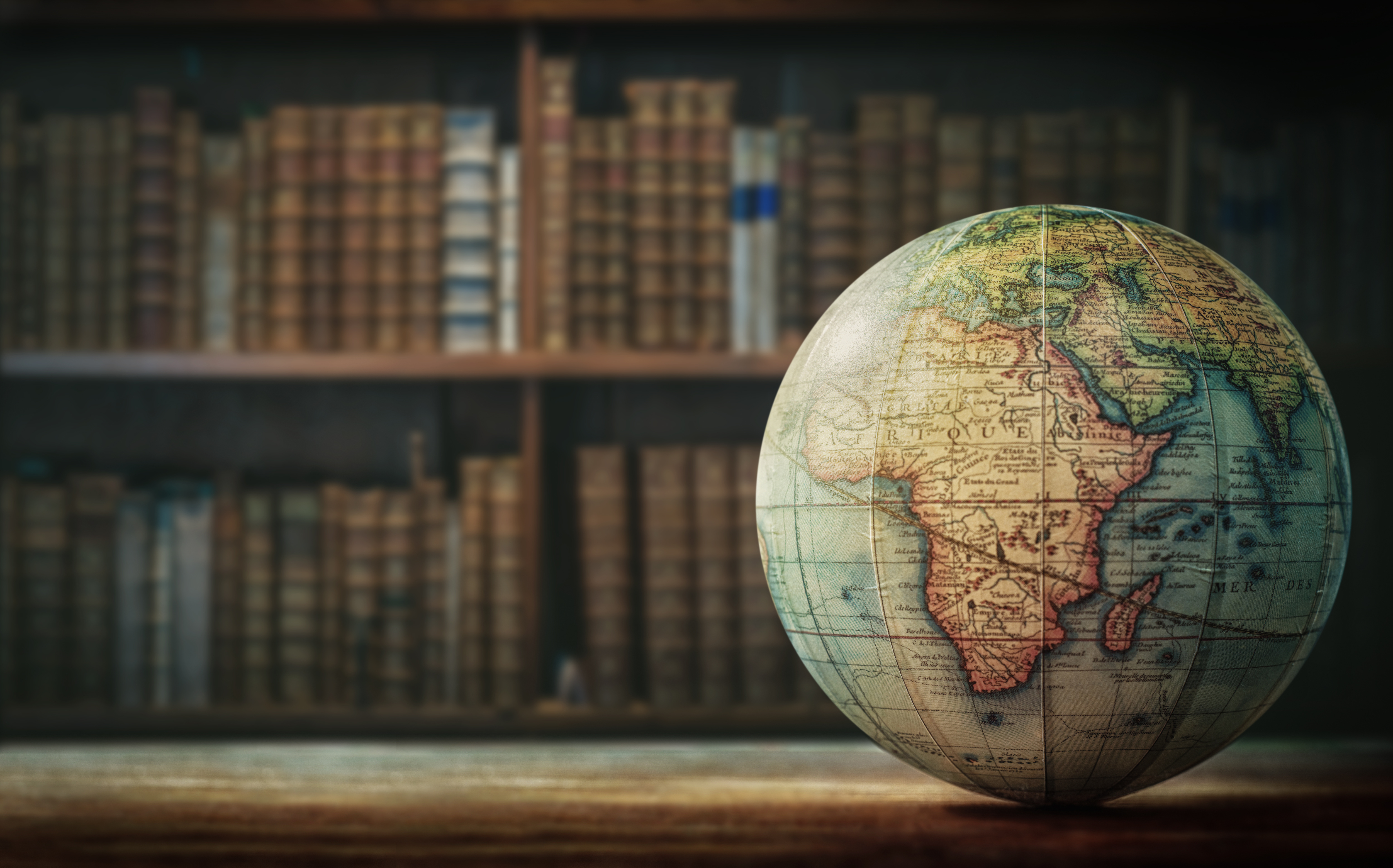 A globe in the foreground with shelves of old books in the background