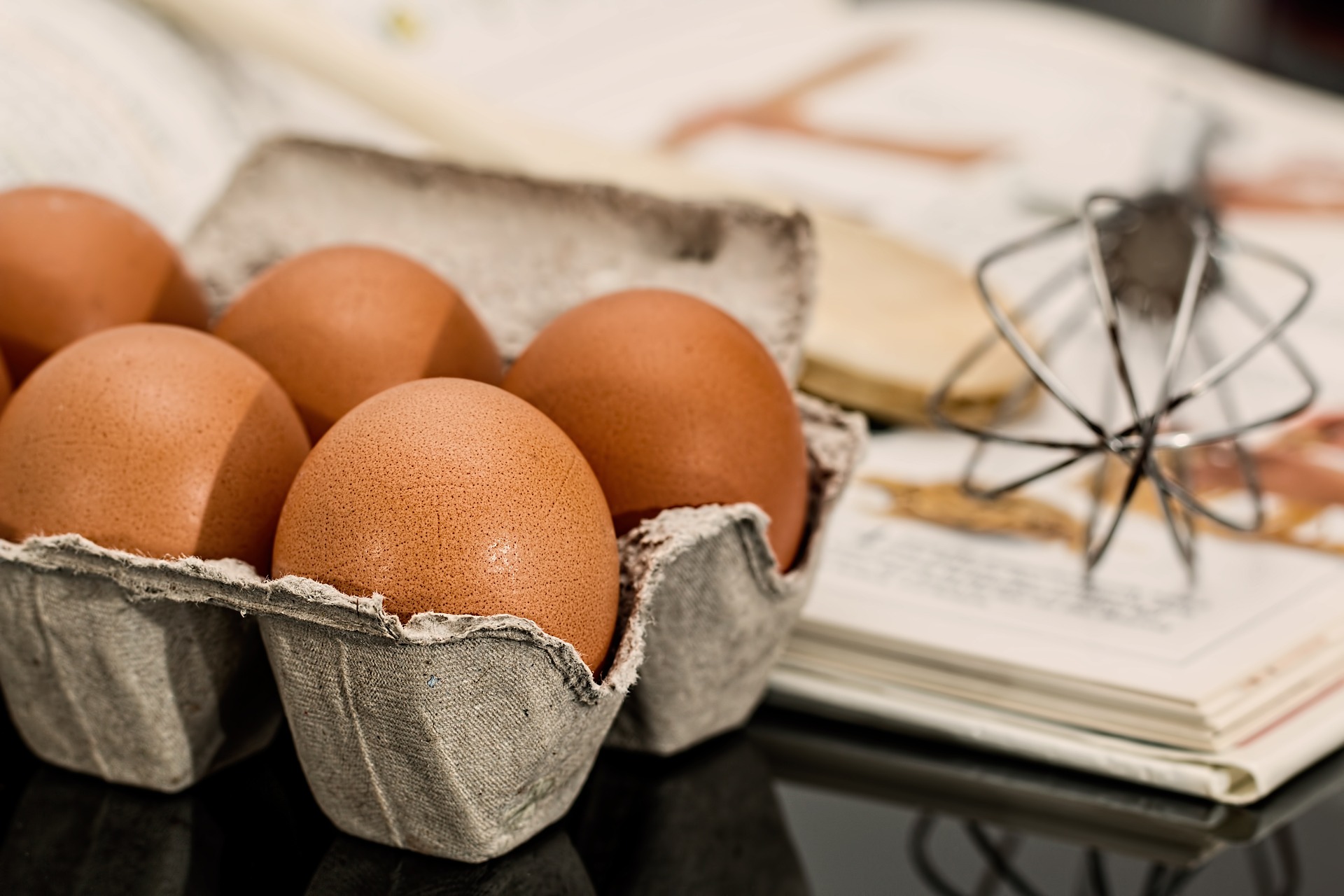 A cookbook, carton of eggs and a whisk