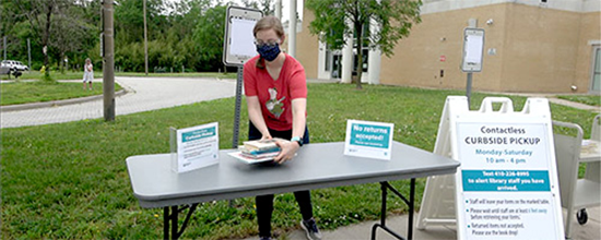 Librarian working curbside pickup table with mask on