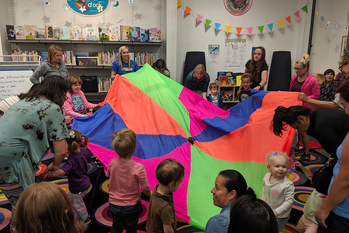 Children playing with rainbow parachute in library