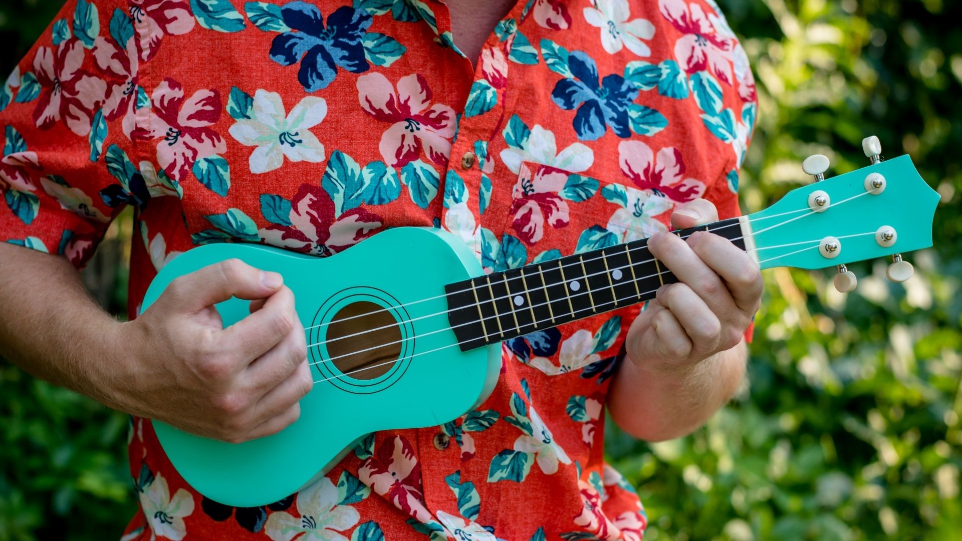 Person in Hawaiian shirt playing a ukulele