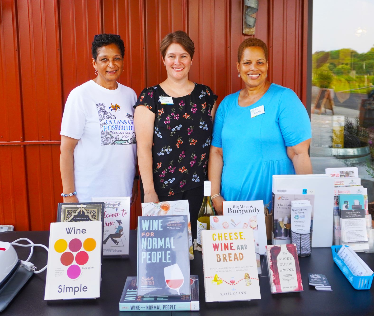 Three librarians from Eastport Annapolis Neck Branch posing for photo behind table displaying books on wine.