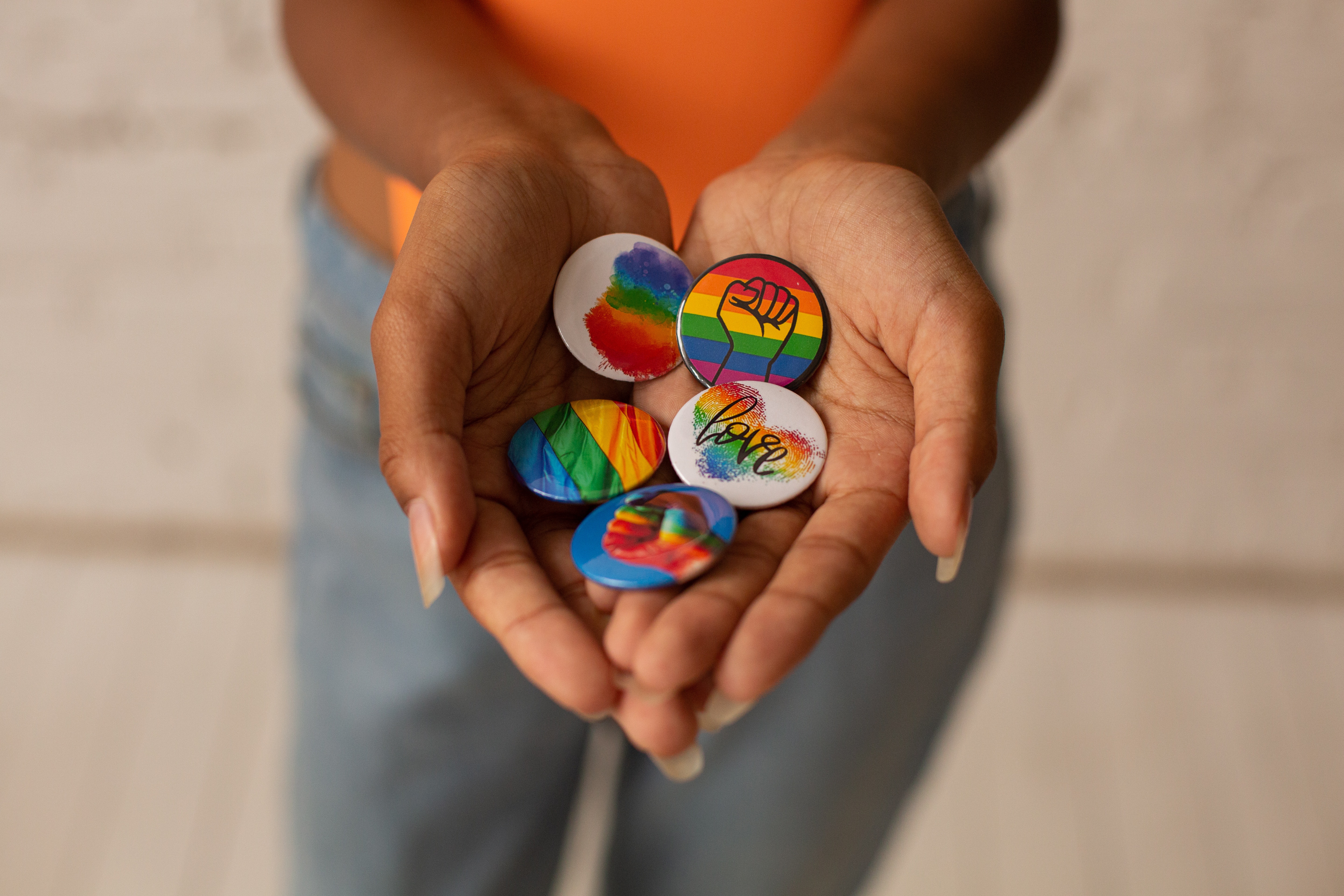 A person holding out a handful of colorful rainbow LGBTQ+ pride buttons. 