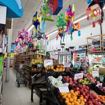 A Latino market with fresh fruits, vegetables, other kinds of food on display, and piñatas hanging from the ceiling. 