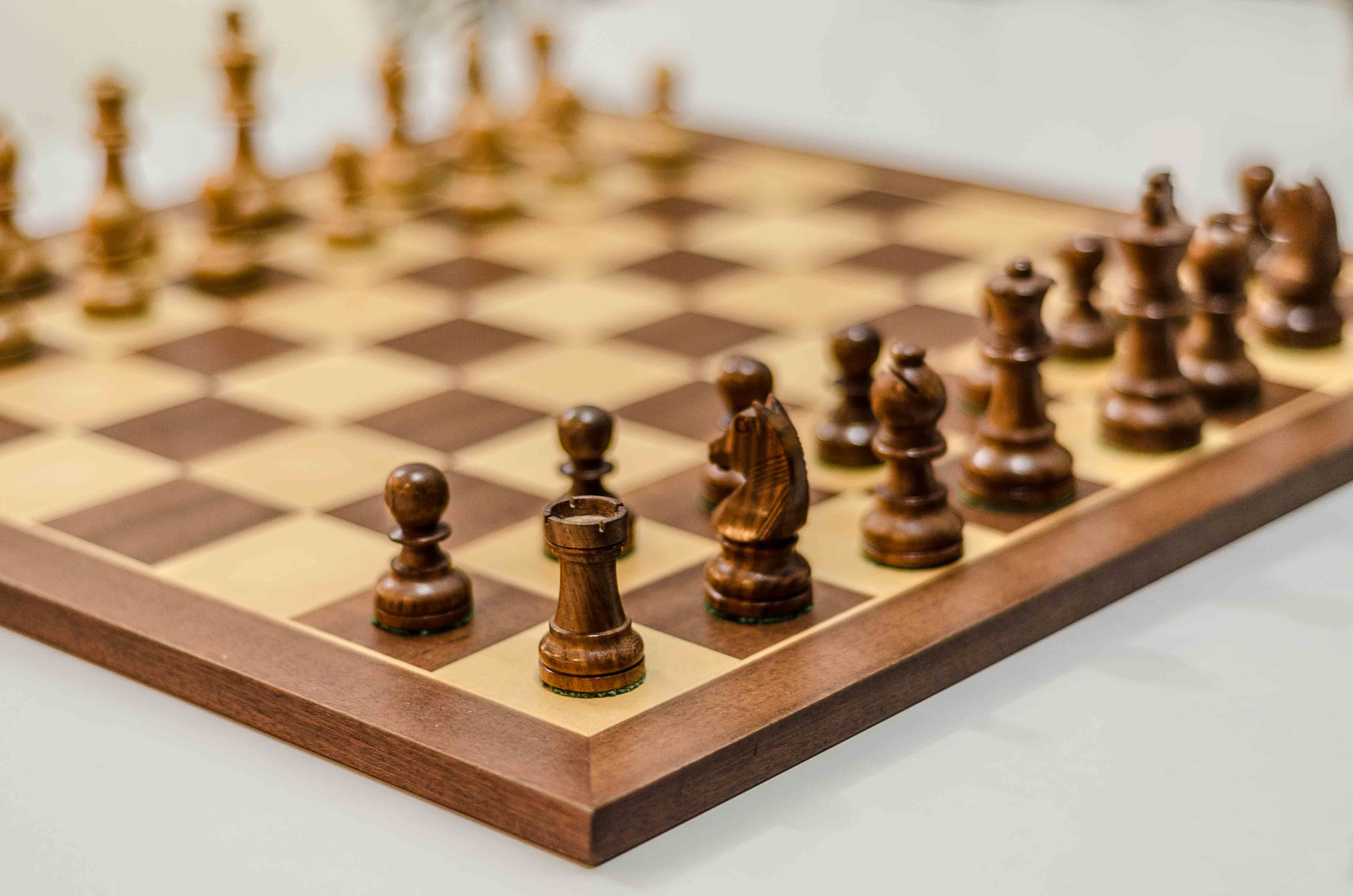 A wooden chess board ready for play, set with tan and maple pieces.