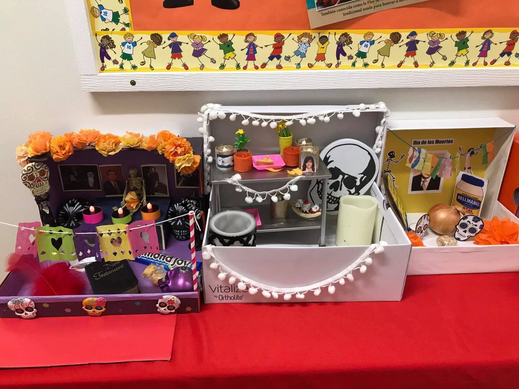 3 SHOEBOX OFRENDAS (ALTARS) REPRESENTING A DECEASED LOVED ONES LIFE. EACH SHOEBOX HAS A PICTURE OF THE LOVED ONE, SUGAR SKULLS, AND OTHER TRADITONAL ITEMS THAT AN OFRENDA USUALLY HAS. 