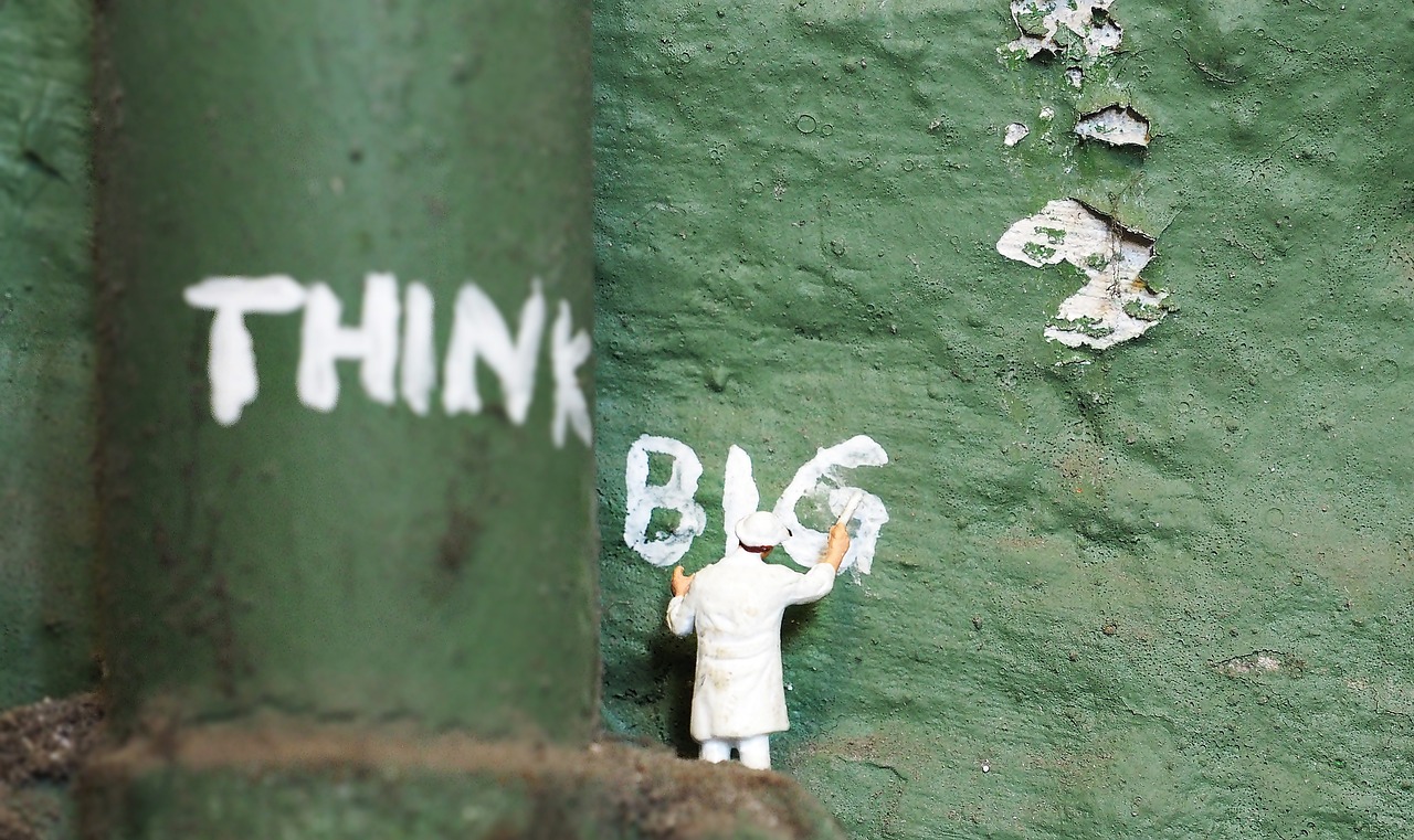 An image depicting a miniature man painting the words "THINK BIG" on a green pipe and green wall. 