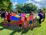 Kids and staff playing outside with a parachute during a Summer Reading Kickoff event at Crofton Library.