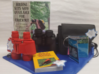 "Birding kits now available for checkout." Red binoculars, black binoculars, Birds of Maryland & Delaware book, and black binoculars case on a blue drawstring bag.