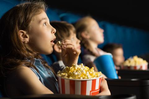 Kids sitting in theater seats and eating popcorn while watching a movie
