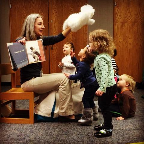 Librarian holding a storybook and a puppet as several small children watch