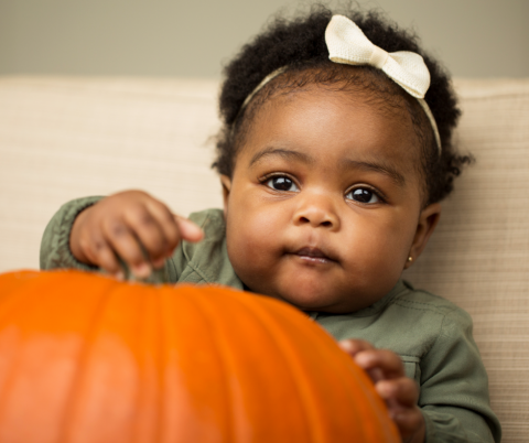 Baby girl with bow in her hair holding onto a pumpkin