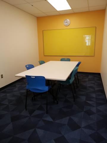 Conference room with table, six chairs and a  yellow whiteboard.