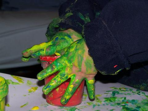 Close up of a baby's hands covered with green paint holding a red bucket