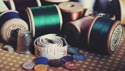 A close-up image of several colorful spools of thread, buttons, and fabric measuring tape. 