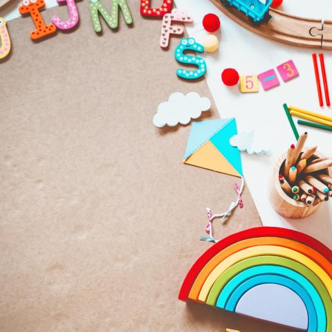 The image shows materials on a surface such as wooden letters and numbers, pencils, paper crafts of a kite, and a rainbow puzzle. 