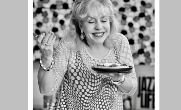 Robin Daumit holding a plate of food while smiling, black and white photo.