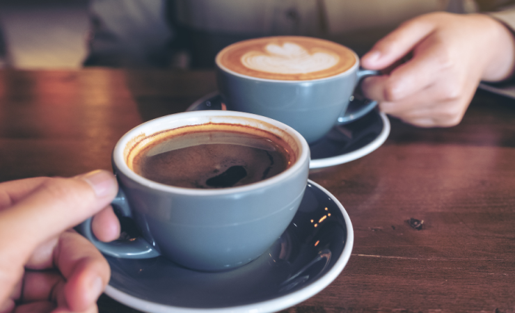 Two cups of coffee being held on a dark wood table