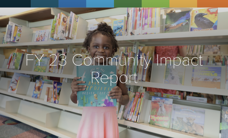 FY23 Community Impact report. Young girl standing in front of a bookshelf holding a book